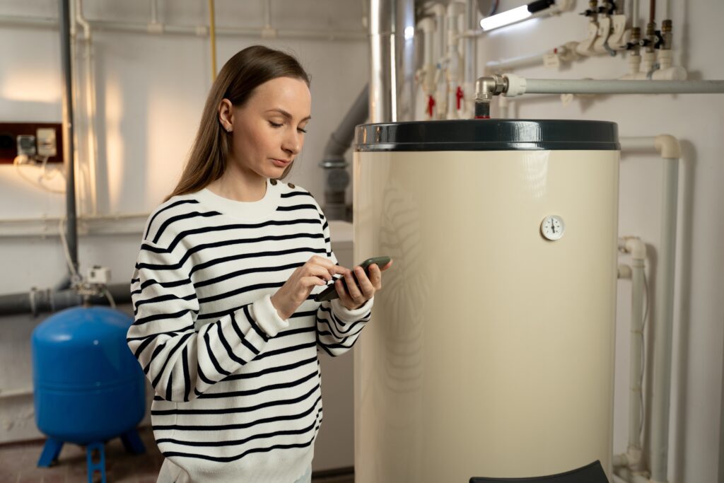Woman using smartphone near a residential hot water tank, showcasing emergency plumbing services, voice search behavior, and mobile-driven local SEO for home service businesses.