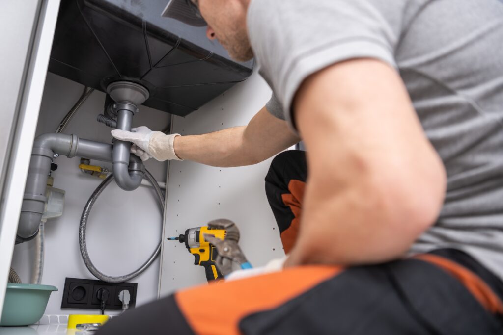 Plumber fixing sink drain under kitchen cabinet, demonstrating plumbing repair services for home service businesses using YouTube ads and Google Local Services.