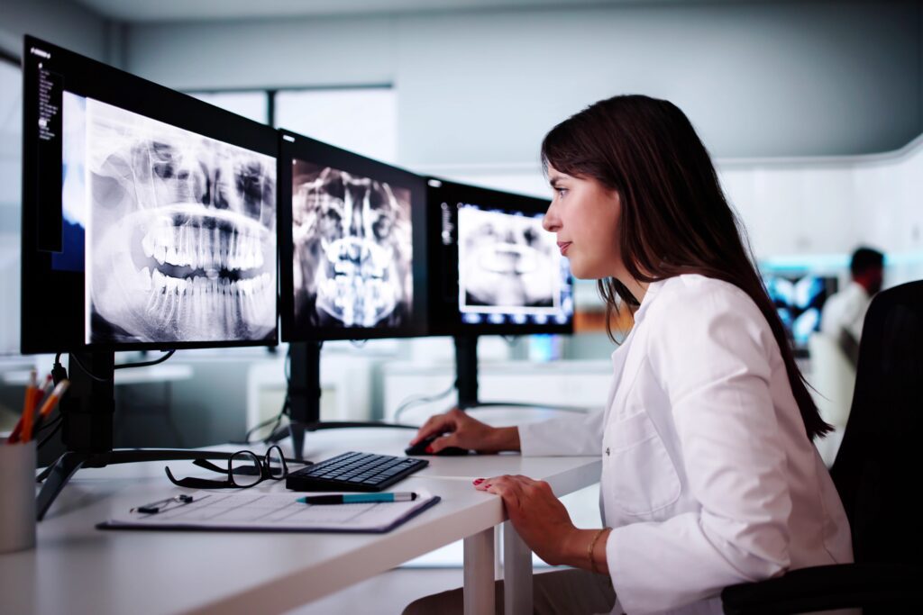 Female dentist reviewing dental imaging on computer screens, representing digital health tools, precision diagnostics, and Google Ads targeting for dental practices and oral surgery campaigns.