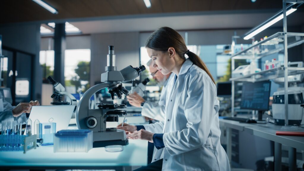 Female biotechnology researcher analyzing samples under microscope in a modern laboratory, symbolizing medical innovation, clinical trials, and digital marketing for pharmaceutical and biotech companies.