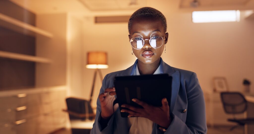 Focused ecommerce professional using a tablet at night to manage digital marketing, automation, inventory, and analytics for bundling and cross-sell strategies.