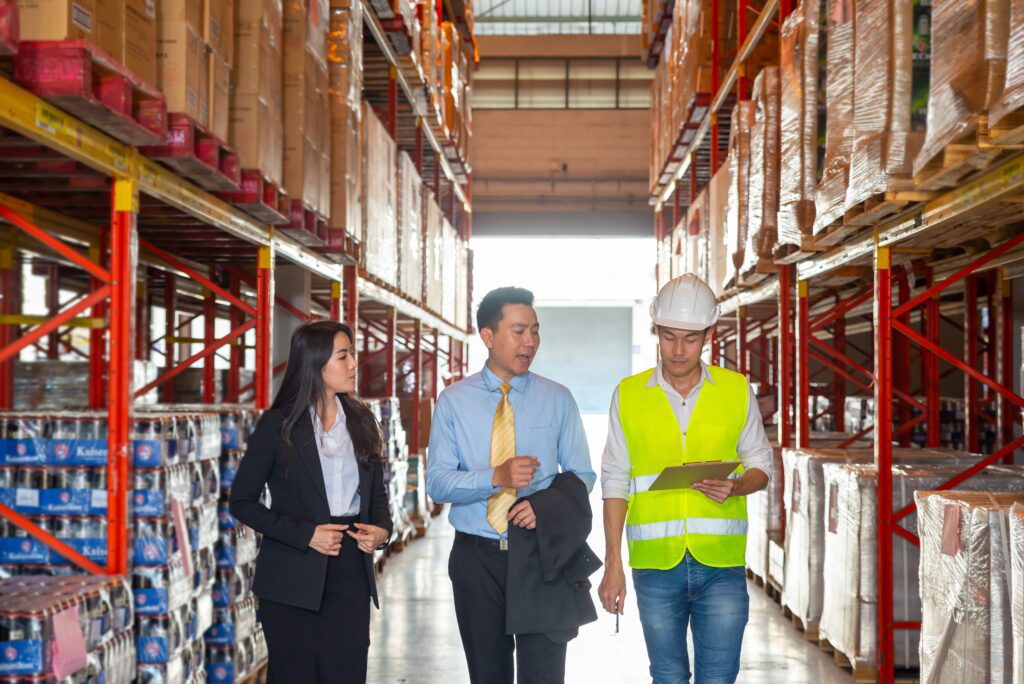 B2B ecommerce executives and warehouse staff reviewing fulfillment operations—highlighting collaboration in supply chain management, retail inventory accuracy, order processing, and customer satisfaction strategies within a warehouse environment.