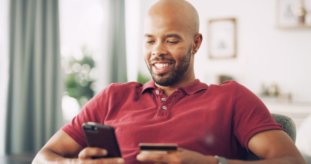 Happy man using smartphone and credit card for mobile shopping, illustrating SMS marketing, ecommerce customer journey, and mobile-first subscription purchase experience.