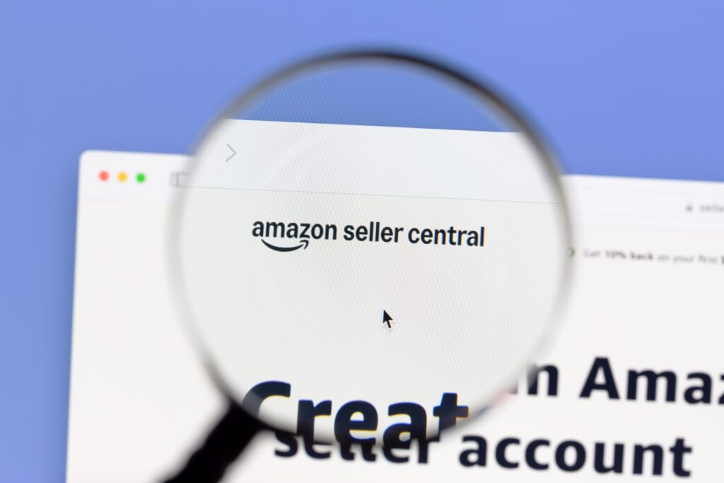 Close-up view of Amazon Seller Central homepage through a magnifying glass, illustrating Amazon FBA, seller account setup, customer feedback management, and ecommerce business tools for product reviews and reputation strategy.