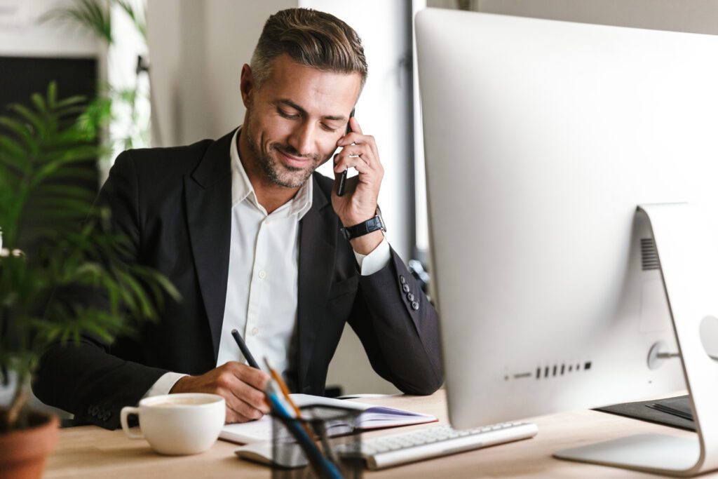Business professional in suit discussing digital marketing strategy on mobile phone while working at desk, representing PPC and SEO lead generation for law firms, consultants, and service-based businesses.