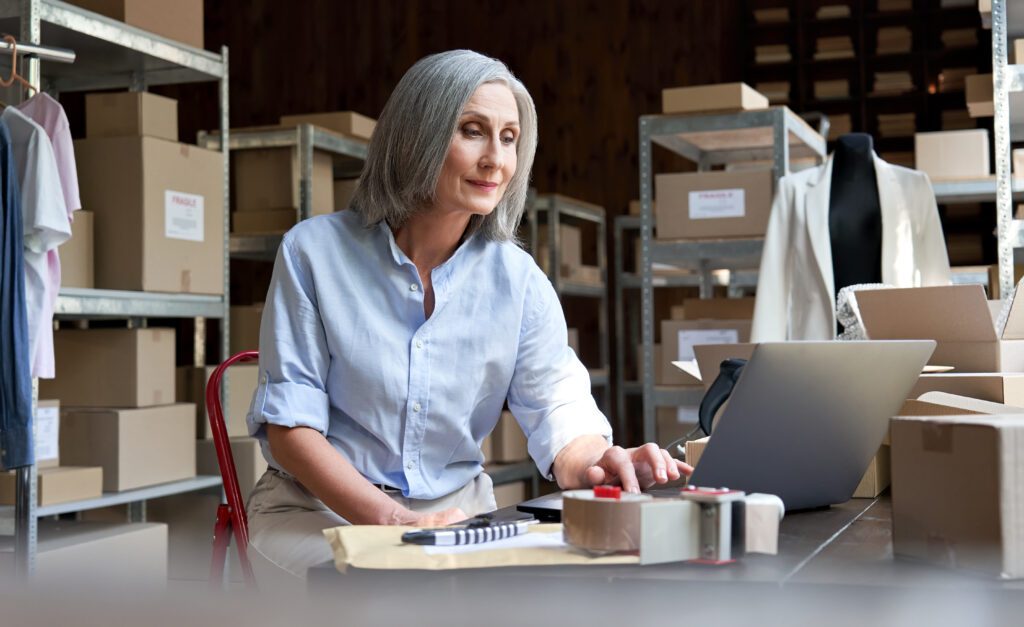 Ecommerce business owner managing online shopping orders and digital marketing tasks on a laptop in a warehouse, focusing on SEO, backlink strategy, and content creation.