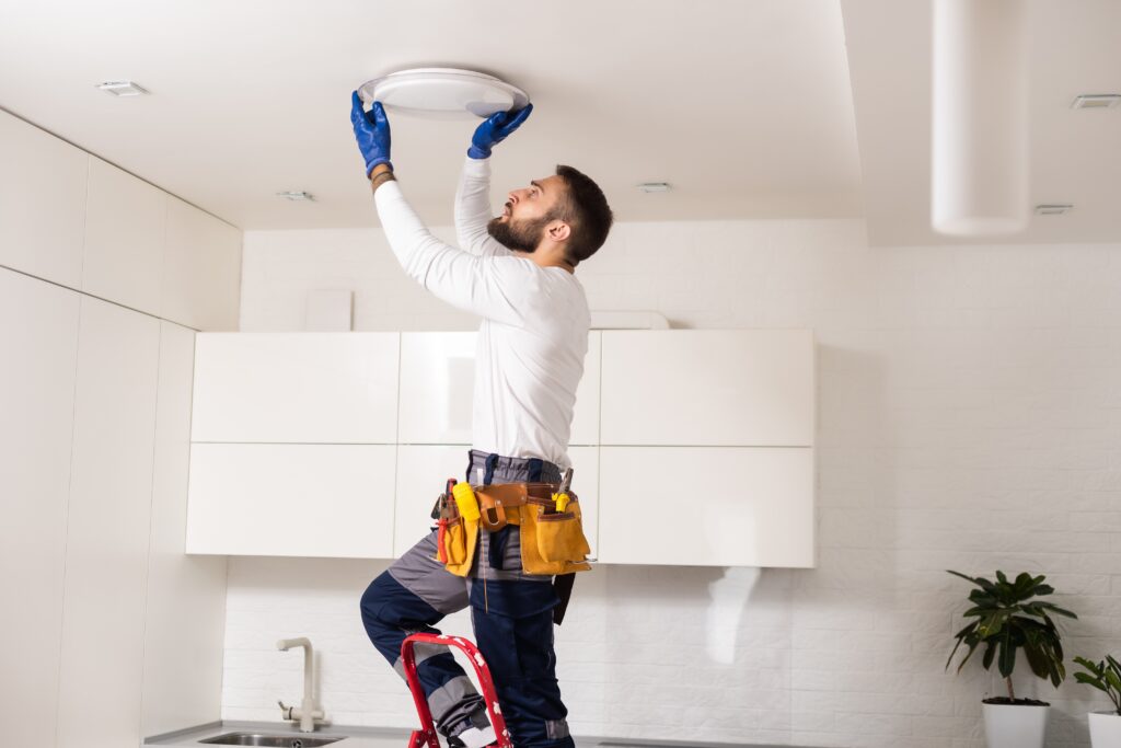 Professional electrician in a modern kitchen installing a ceiling light fixture, demonstrating expert home service skills and the importance of local SEO and digital marketing for electricians.