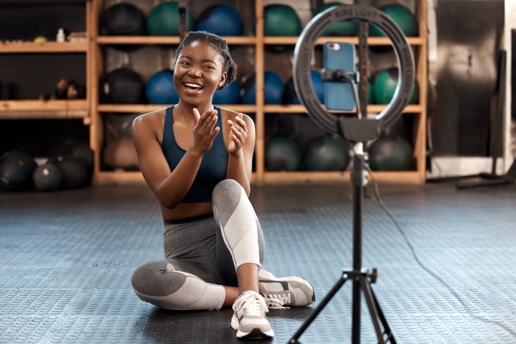 Personal trainer creating TikTok fitness content in a gym using a ring light and smartphone, promoting digital marketing, physical fitness, and social media engagement for health and wellness brands.