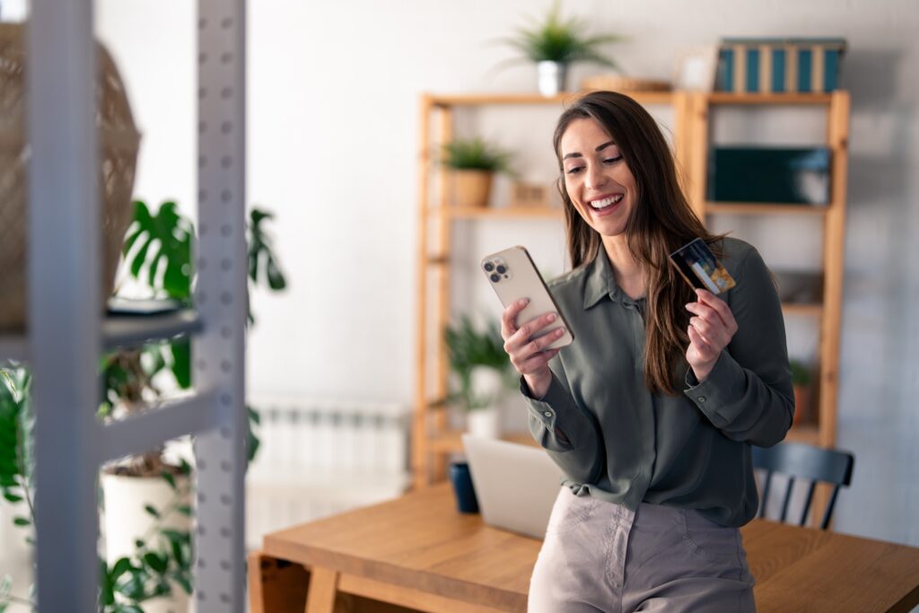 Smiling woman making a mobile ecommerce purchase with her smartphone and credit card, highlighting mobile commerce optimization and secure payment experience.