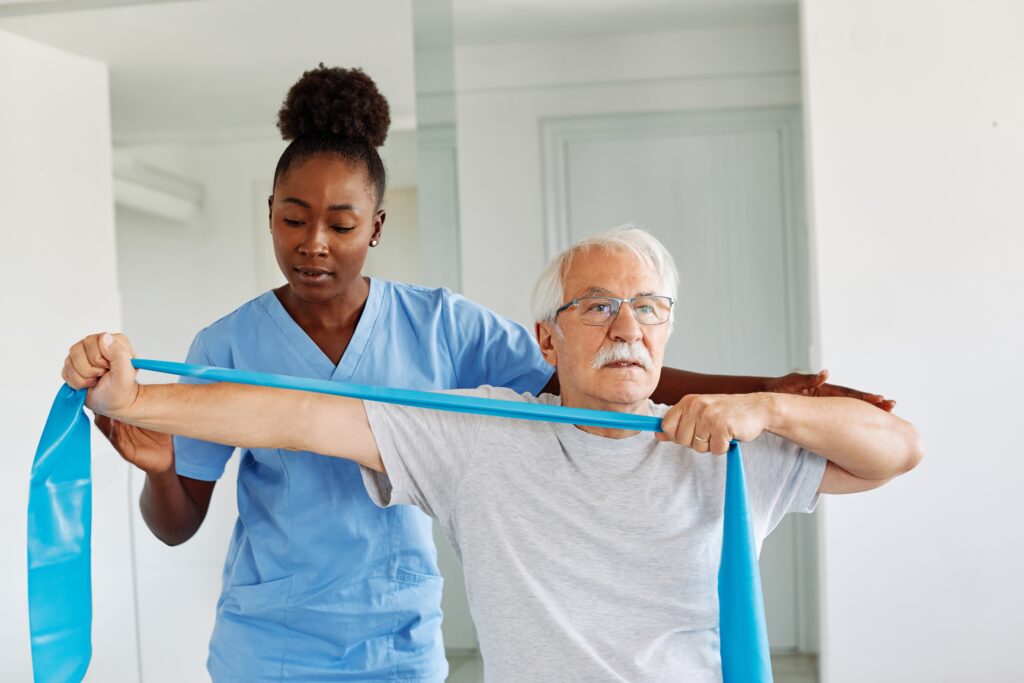 Physical therapist assisting an elderly male patient with resistance band exercises during a rehabilitation session, highlighting patient-centered care, physical therapy services, healthcare marketing, and the importance of trust and social proof in senior wellness and recovery programs.