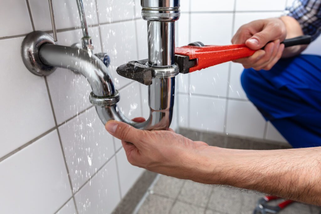 Plumber using a red pipe wrench to stop a leaking pipe, symbolizing emergency plumbing services and the importance of targeted advertising and digital marketing for plumbers.