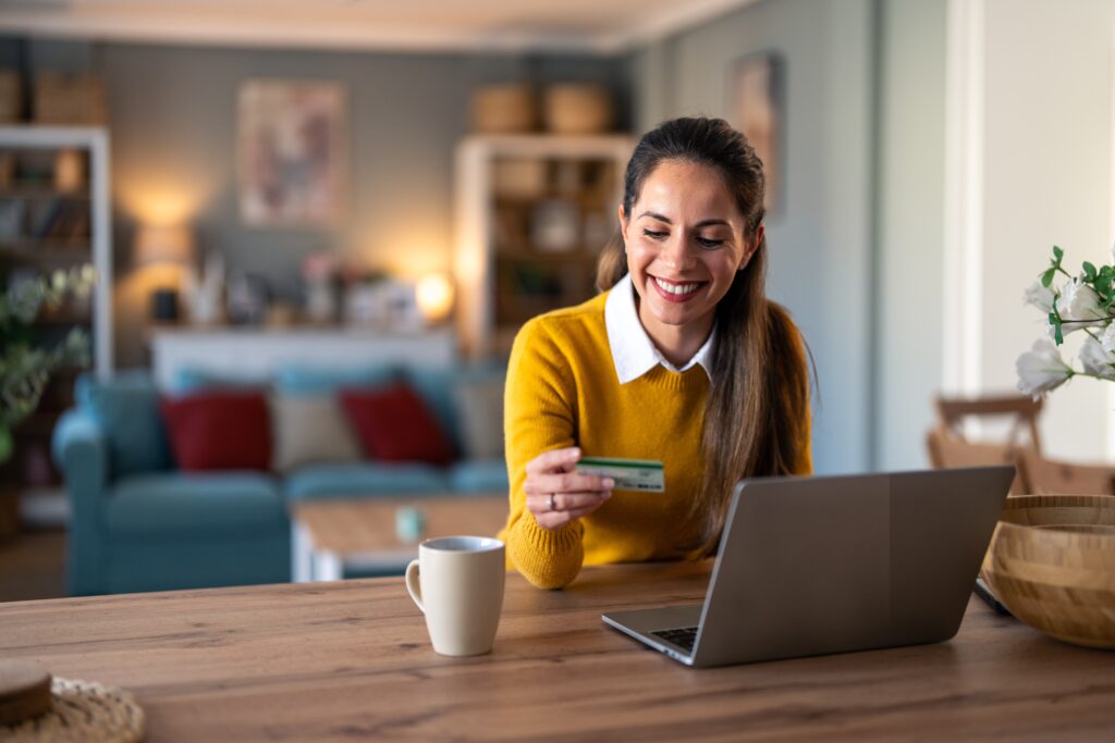 Smiling woman shopping online with laptop and credit card, representing ecommerce customer experience and online shopping for Shopify and WooCommerce stores.